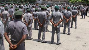 A large formation of Nigerian Navy and Customs Service personnel standing at attention on a parade ground, in full uniform, with the RTCOM Defense logo overlaid in the upper corner and a bold headline card reading: "NAVY, CUSTOMS SEIZE 518 BAGS OF SMUGGLED RICE" — documenting a joint interdiction operation conducted on 31 July 2026 following intelligence generated by the Falcon Eye maritime and border surveillance system.