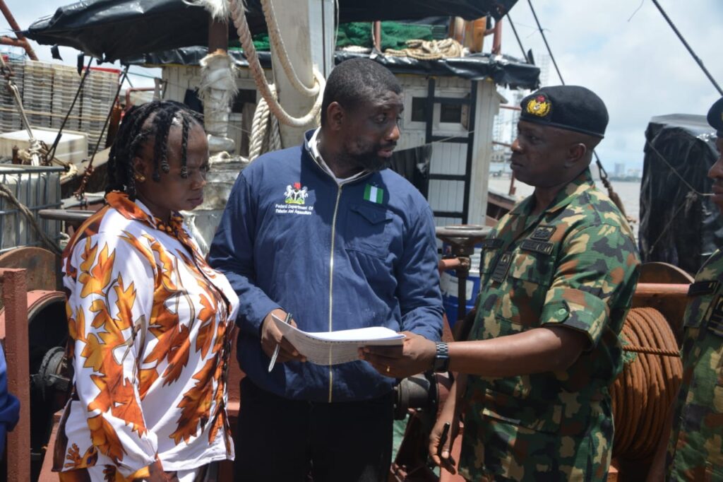 Nigerian Navy officer handing over seized illegal fishing vessel documents to a Federal Department of Fisheries and Aquaculture official aboard a ship.